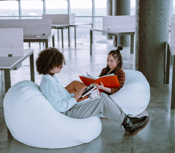 two women sitting on bean bag chairs reading books