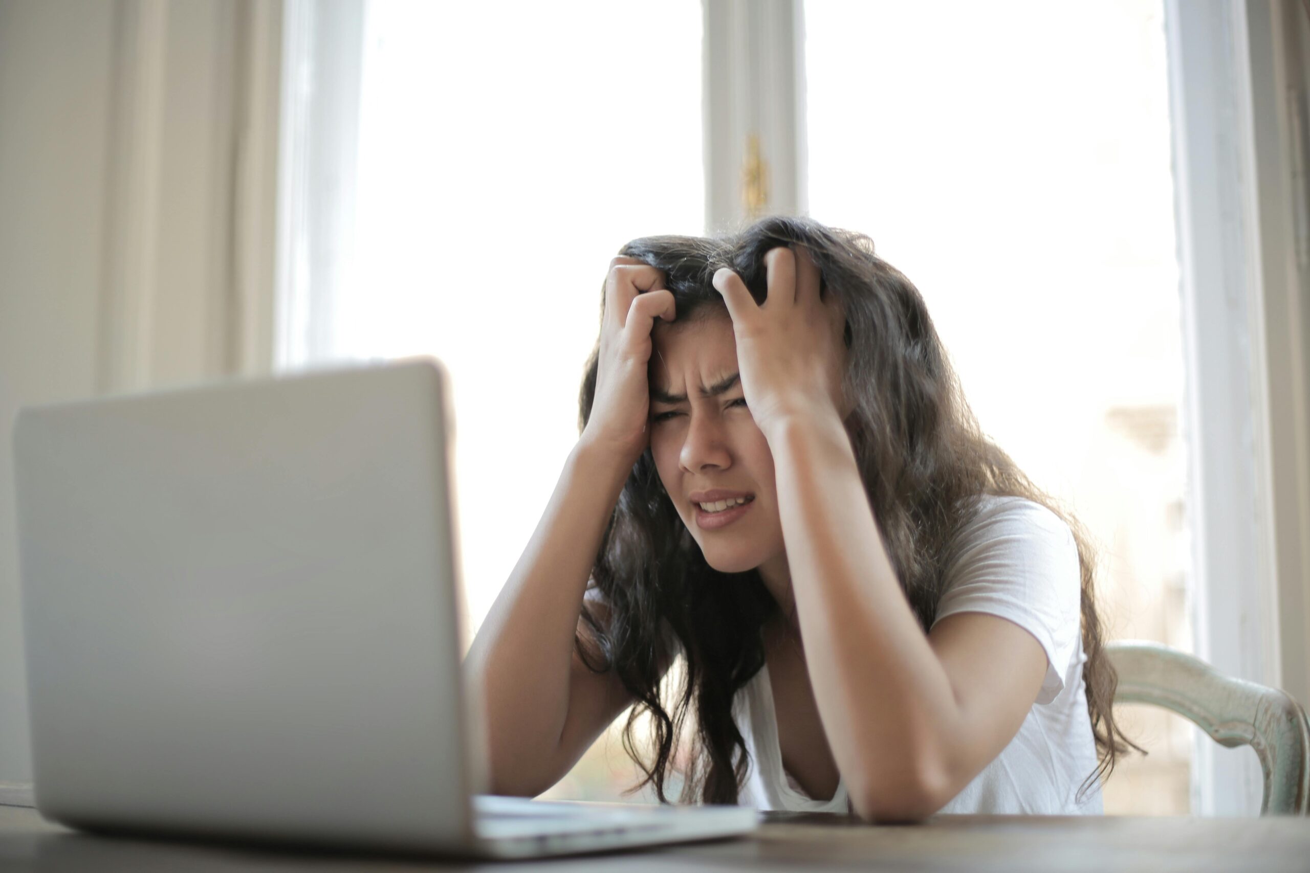 A woman is holding her head in front of her laptop. frustrated with long covid